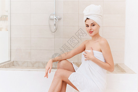 一位微笑的年轻妇女洗完澡后照顾她的皮肤和头发 在家中进行淋浴治疗 提供皮肤护理化妆品女孩洗澡镜子卫生女士浴室毛巾成人温泉图片