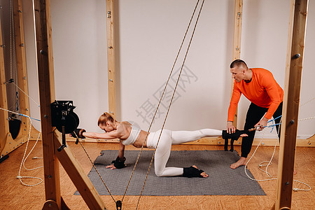 一名教练将身穿运动制服的女孩拉在人体伸展的模拟器上力量身体压力训练运动员紧张肌肉绳索男人牵引力图片