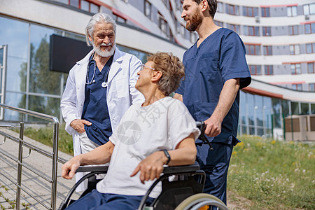 护士和医生步行时在医院院子里与轮轮椅病人交谈护理女士老年轮椅人士车轮诊所椅子成人退休图片
