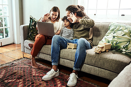 向相机挥手 一对开朗的年轻夫妇和他们的儿子坐在家里的沙发上 用笔记本电脑给亲戚打视频电话图片