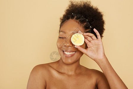 美丽的美籍女性模特儿在米色背景上将半个柠檬放在脸前 用维他命C 皮肤护理和SPA来照顾化妆品的概念图片