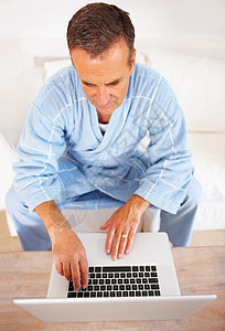 一位穿着浴袍的老人在家里用笔记本电脑工作 一位在家使用笔记本电脑工作的退休老人的俯视图图片