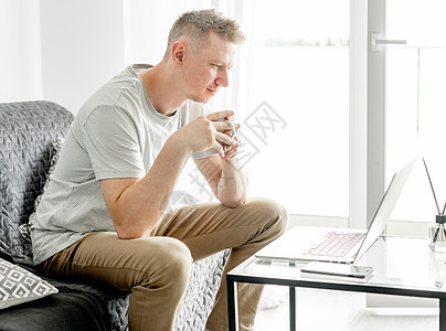 英俊的年轻人在笔记本电脑上工作工作者互联网办公客厅网络远程键盘白色沙发男人图片