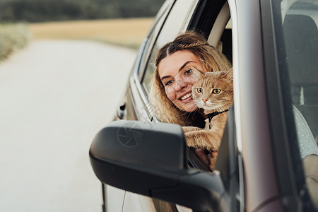带着红猫从车窗向外看的白种年轻女子 同时享受周末公路之旅图片