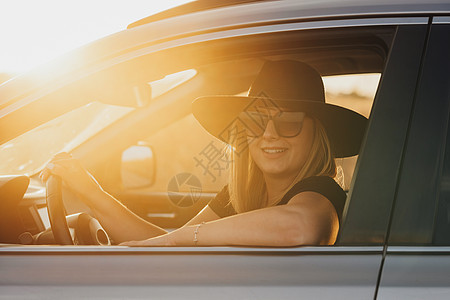 日落时开着车 穿着帽子和太阳眼镜驾车的年轻快乐女子肖像图片