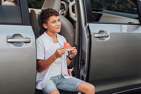 白种白人少年男孩坐在Minivan汽车上吃西瓜 带着笑容往前看图片