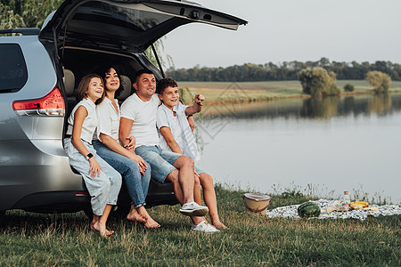 坐在Minivan汽车Trunk的四位高加索快乐成员家庭 母亲和父亲与两个少年儿童一起坐在Lake湖边有周末辣椒门的儿女图片