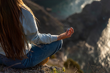 女性游客享受海山地貌的日落 坐在海面上的岩石上户外 穿着牛仔裤和蓝色连帽衫 健康生活方式 和谐与冥想 续假期杯子喜悦自由太阳海洋图片