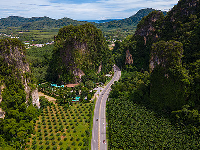 泰国Krabi棕榈树和石灰岩山之间交通畅通的美丽道路沥青农村蓝色森林天线街道热带小路游客树木图片