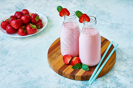 草莓冰沙或奶昔放在玻璃罐里 有蓝水泥底的浆果薄荷饮食奶制品小吃早餐稻草液体食物甜点牛奶图片