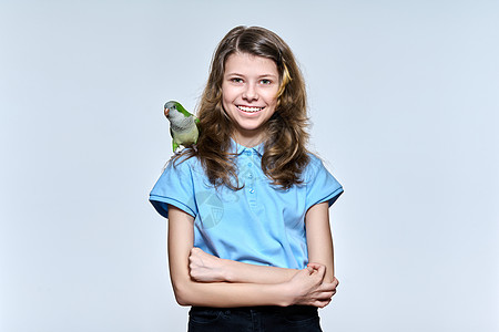 带着宠爱的绿色石斑鹦鹉的女孩 在轻光工作室背景上观看摄影机成人羽毛情调贵格女性宠物孩子动物热带友谊图片