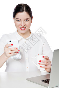 穿着白衬衫坐着 拿着一杯饮料 智能手机和带着牙齿笑容看的美丽黑发女商务人士的快乐成功光辉肖像图片