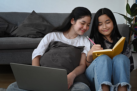 两个微笑着的亚洲女孩在互联网上上网 或在客厅用笔记本电脑做家庭作业图片