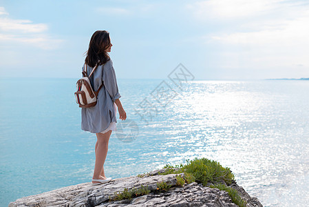 一个穿夏衣旅行的女孩 穿着时装背包 在海边的白色岩石上玩海滩太阳自由喜悦支撑海岸乐趣假期幸福衣服图片