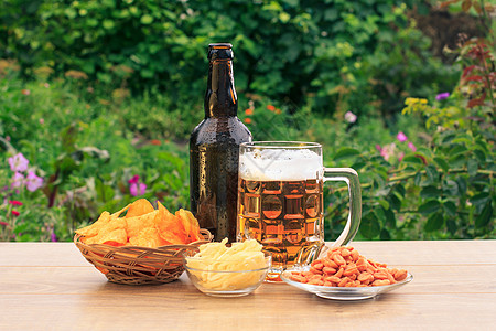 一杯啤酒和一瓶啤酒加土豆薯片在木制桌上图片