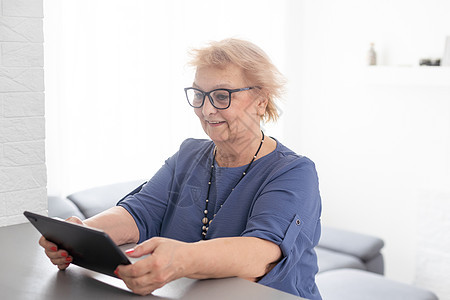 快乐成熟的中年女性在家里使用数字平板电脑度过闲暇时光 性格开朗的现代高级女士拿着电脑 看有趣的电影和笑声 休闲和科技理念购物摄像图片