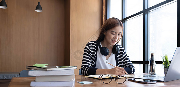 微笑的亚洲本科少女学生在图书馆学习 笔记本电脑书籍为课程作业进行在线研究 为论文作业做笔记 在线教育电子学习概念女性说话课堂麦克图片