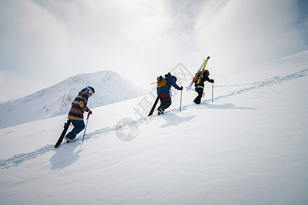 三个玩滑雪的朋友滑雪者上山 用雪板和滑雪机在他们的手中为后国或搭便车而跳雪男人高山活动假期远足顶峰蓝色运动粉末季节图片