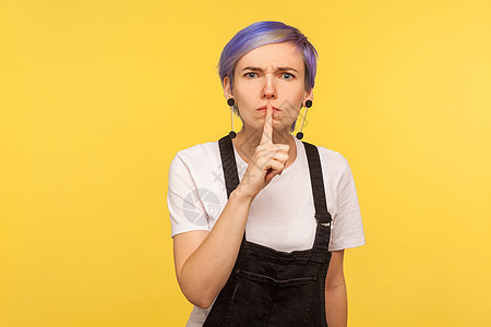 黄色背景的情绪时髦女人的肖像工人愤怒老板背叛嘴唇女孩惊喜牛仔手势背带裤图片