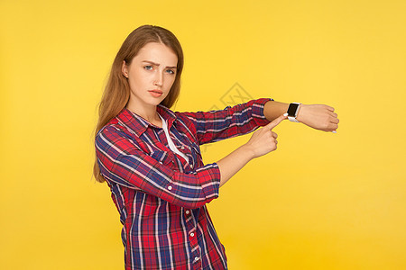 黄色背景的年轻情感女性的肖像手势女孩女士手表小时老板警告衬衫格子手指图片