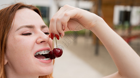 美丽的红发年轻美女 牙齿上戴着牙套 在夏日户外吃甜樱桃阳光植物果园饮食水果快乐食物浆果女性甜点图片