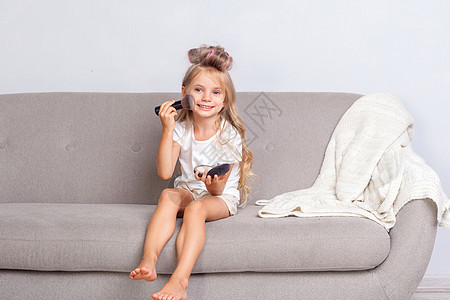 可爱的小女孩 头发卷曲 坐在沙发上化妆 对着镜头微笑图片