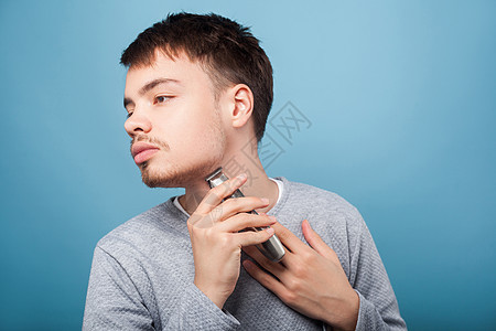 蓝色背景的年轻男子的美容和保健剃刀混血卫生发型男性护理脸颊黑发毛衣理发店图片