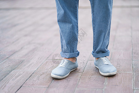 穿着牛仔牛仔裤和运动鞋的时尚男子脚 在街上大理石或陶瓷板上单独露在外面图片