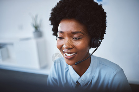 一位快乐的年轻非洲裔美国呼叫中心电话营销代理在办公室用电脑工作时戴着耳机交谈 面对自信友好的女性顾问操作客户服务和销售支持帮助台图片