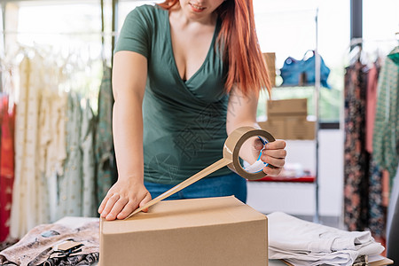 一位年轻女商务人士的剖视图 她正在用胶带包装一个盒子 以便从她的网上服装店发货 年轻女子在办公室为客户准备包裹 工作和经营理念图片