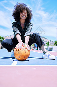性格开朗的年轻非洲女性 一头卷发的爆炸头蹲在球场上 手里拿着篮球 正在外面打篮球的微笑女人的画像 快乐享受篮球图片