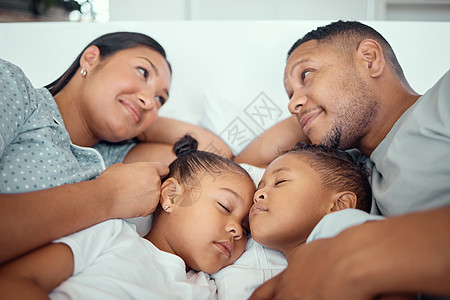 慈爱的父母在拥抱他们的两个孩子时互相看着对方 睡在父母床上的小女孩和男孩图片