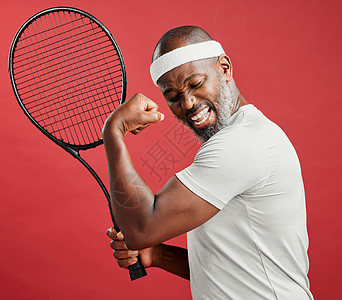 一个快乐的成熟非洲裔美国人站在工作室的红色背景下 一边用网球拍摆姿势 一边弯曲二头肌 微笑的黑人在比赛时感觉健康和运动图片