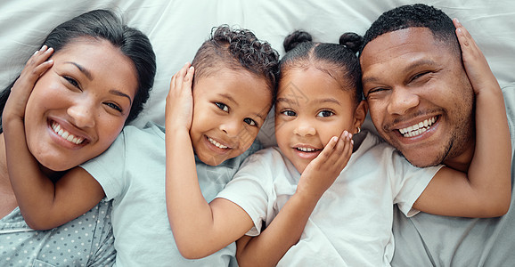 快乐的混血家庭的肖像 有两个孩子在家里放松并躺在床上 从上面看 弟弟和妹妹手放在对方脸上 同时与他们慈爱的父母亲近图片