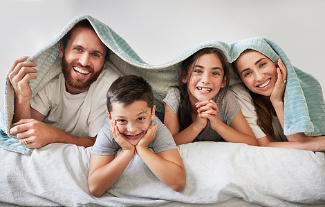 幸福的白人四口之家的肖像躺在床上 头上盖着毯子 无忧无虑的父母在周末与他们的女儿和儿子一起度过空闲时间 微笑的家人躺在床上享受懒图片