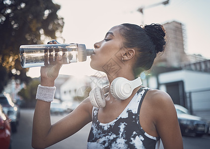 一位健康的年轻混血女性在户外锻炼时休息一下 从瓶子里喝水 女运动员在城市跑步训练后解渴降温图片