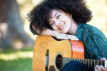 微笑的年轻音乐家在公园玩耍和享受一天时 靠在她的原声吉他上休息 快乐的西班牙裔女人 一头卷发 在外面的花园里用吉他弹奏音乐图片