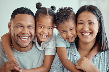一个快乐的年轻混血家庭的肖像 两个孩子穿着睡衣坐在家里 可爱的小女孩和男孩从背后拥抱他们的父母图片