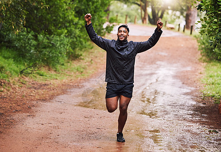 年轻的西班牙裔健美男运动员在大自然中的雨中在森林里奔跑时 用拳头在空中欢呼 锻炼有益于健康和福祉 很高兴达到他的健身目标图片
