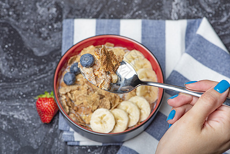 Muesli 早餐 健康食品和饮食Muesli 在黑大理石顶上一块盘子上加牛奶和水果妇女用勺子握手食物营养蜂蜜谷物浆果女士奶制品图片