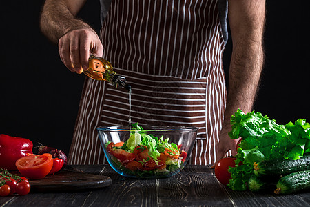 鱼肉沙拉烹饪与家庭概念     特写男性手在碗里加橄榄油的沙拉蔬菜男人成人厨房勺子围裙午餐盘子木板饮食背景