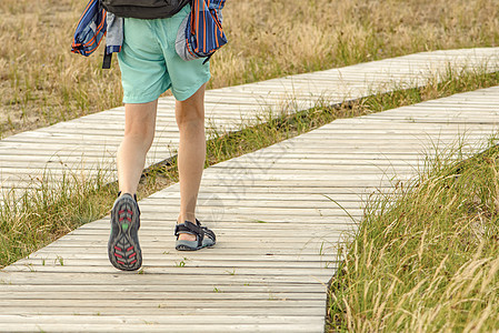 山中的木栈道 蜿蜒的旅游路径由山中的木板制成 一个 10 岁年轻人的腿背着背包沿着旅游路线近距离上山图片
