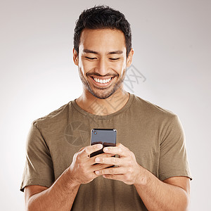 英俊的年轻混血男子站在灰色背景下孤立的工作室里使用手机 西班牙裔男性发送短信 使用互联网或浏览社交媒体图片