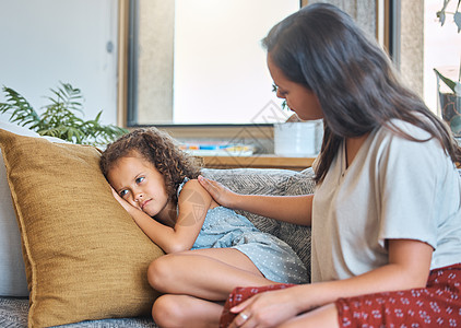 悲伤沮丧的小女孩躺在沙发上 看着别处 而担心的母亲心理学家试图与她交谈 慈爱的母亲试图与心烦意乱的女儿沟通 年轻的西班牙裔母亲在图片