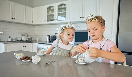 两个小女孩在家里开茶话会 兄弟姐妹朋友在厨房的桌子上玩茶具和吃饼干时戴着头饰 姐妹相处和一起玩孩子朋友们乐趣杯子兄弟游戏青年玩具图片