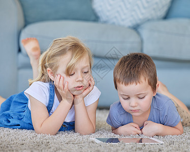年轻的白人男孩和女孩躺在家里的地毯地板上 在线观看卡通视频 在数字平板电脑上玩有趣的游戏 从教育应用程序中学习 使用智能小工具的图片