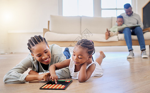 非裔美国人家庭在家里的休息室里聚在一起 黑人母亲和她的女儿在玩游戏 而一个小男孩正在和他的父亲一起读书 家庭玩得开心图片