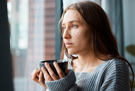 一杯热茶来舒缓灵魂 一个不快乐的年轻女人在望窗外时喝茶的照片 -图片