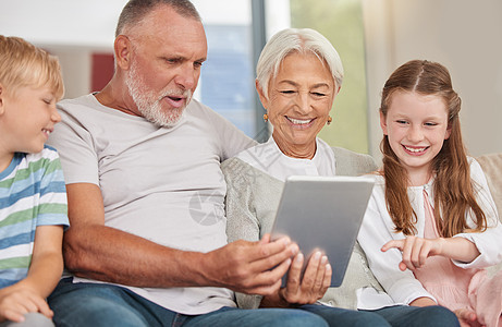 一对快乐的成熟夫妇在家里照顾孩子和使用数字平板电脑时与他们的孙子们在一起 祖父母和他们可爱的小孙子和孙女一起放松浏览互联网图片