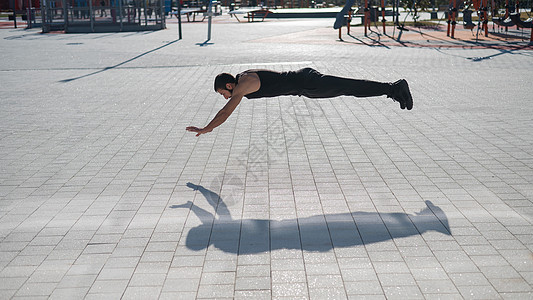 一个穿黑色运动服跳跃的男人 在公园做俯卧撑技术男性地面娱乐重量肌肉健身房全身胡子飞行图片